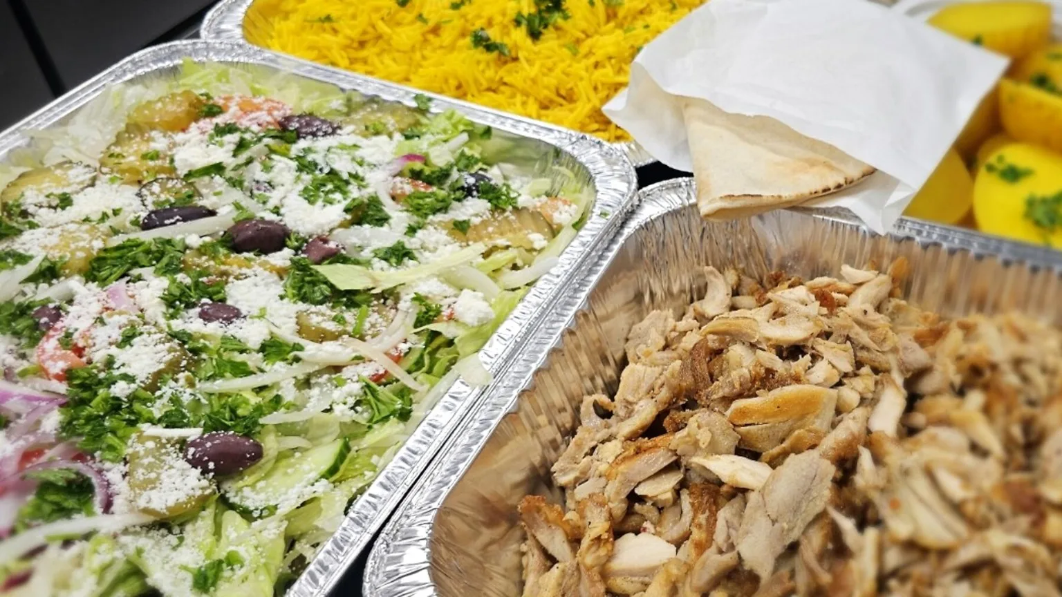 Chicken shawarma, salad, rice and pita in catering trays.