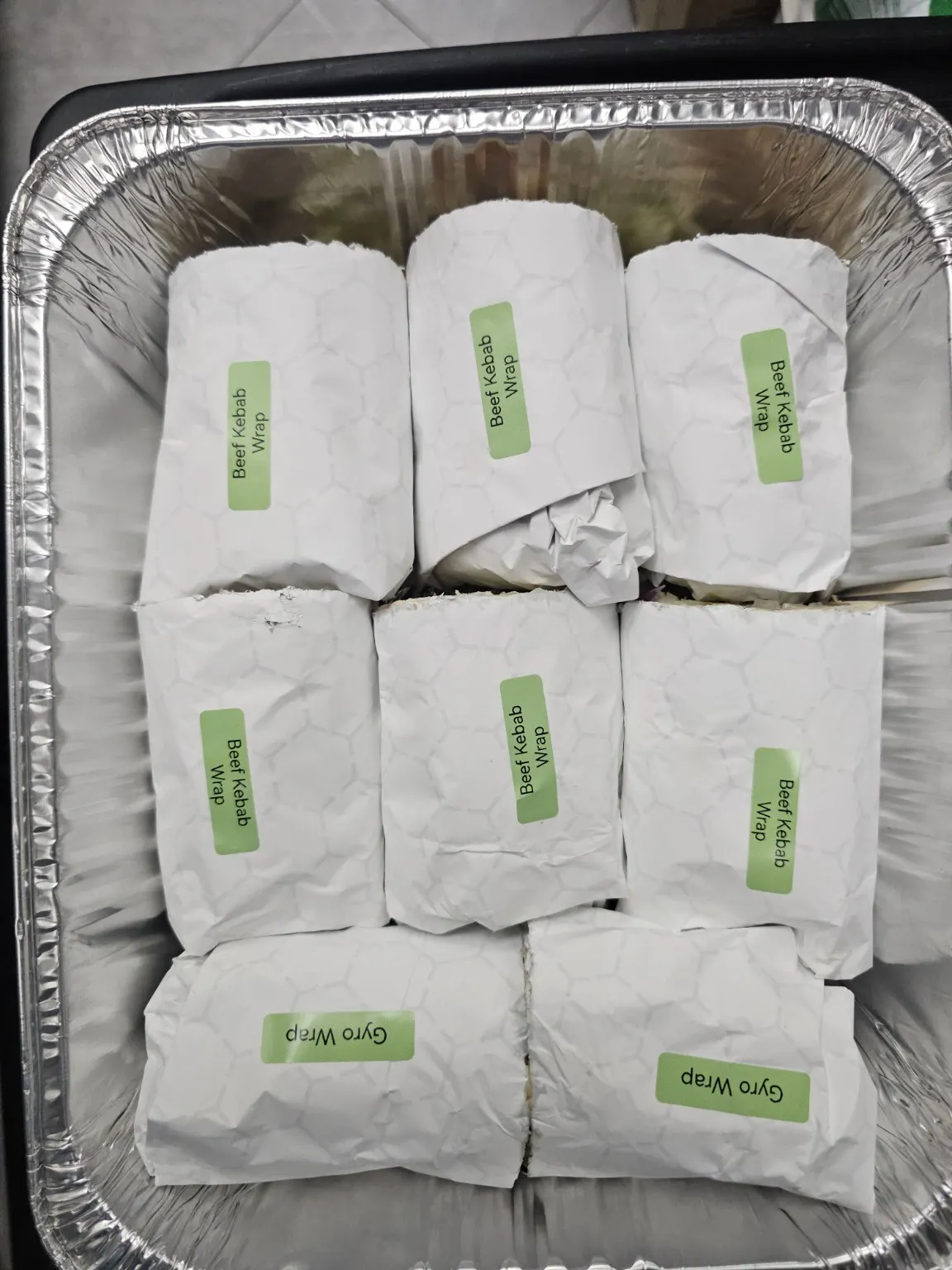 Foil tray of paper-wrapped wraps labelled beef kebab and gyro, from the Pita Lite Eastgate Square Hamilton meeting order.