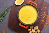 Lentil soup in a serving pot with lemon and bread nearby.