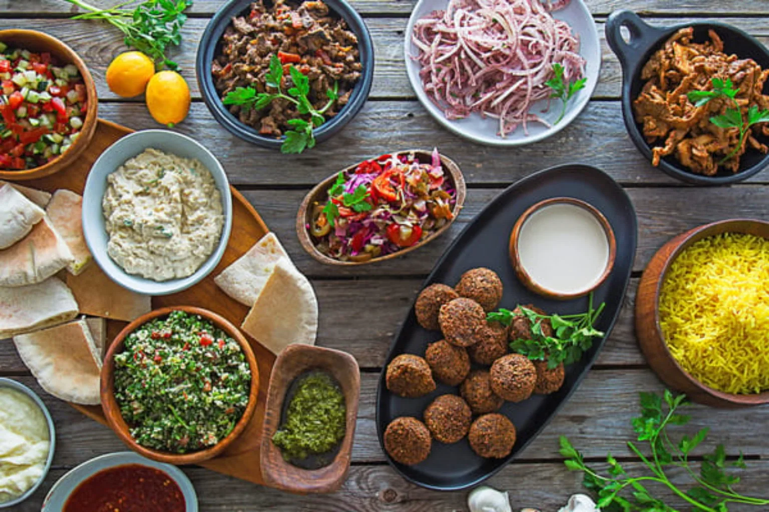 Falafel, rice, salads, pita and dips arranged on a wooden table.